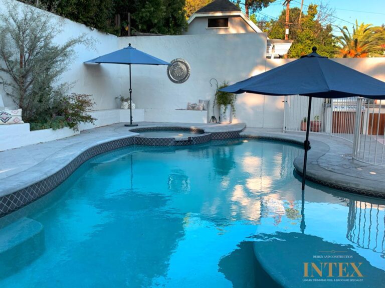 Outdoor pool with blue umbrellas and seating.