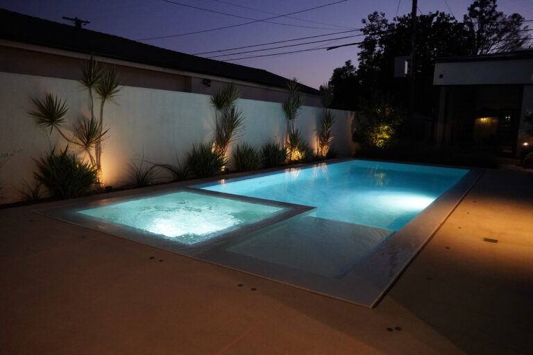 Modern backyard pool and spa at night.