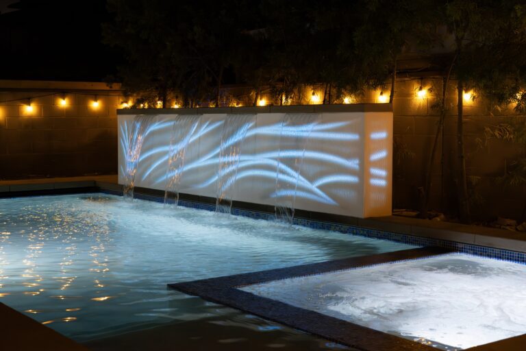 Illuminated pool with waterfall and lights.